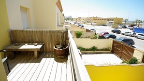 Un balcone con una panchina di legno e piante in vaso, con vista su una strada con auto parcheggiate e edifici.