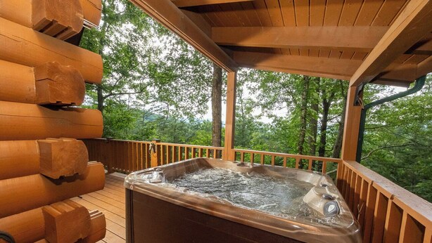 Un jacuzzi en una terraza de madera con vistas a árboles.