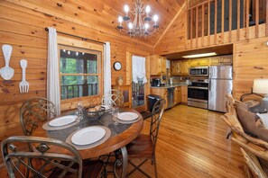 A wooden cabin interior with a dining area, kitchen, and a loft bedroom.
