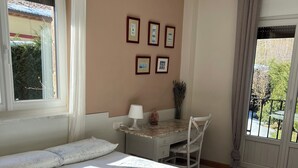 Un lit bien fait, avec une literie à motifs floraux, un bureau avec une lampe et des tableaux encadrés accrochés au mur.