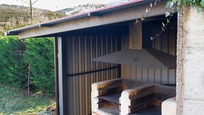 Un espace barbecue extérieur de style rustique, doté d’une cheminée, entouré d’une structure en béton et surmonté d’un toit en métal.