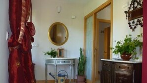 Un couloir avec un rideau rouge, un miroir rond, une petite table avec une plante, une plante en pot et un meuble.