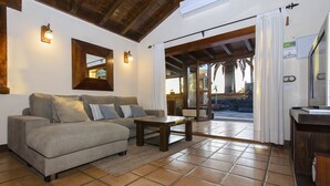 Un salón con sofá, una mesa de centro y vistas a un área exterior con un muro de piedra y palmeras.