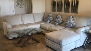 Ein Wohnzimmer mit einem Ecksofa, einem Glastisch und einem Deckenventilator.