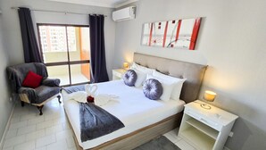A hotel room with a bed, a chair, a nightstand, and a window. - Gray Apartment Praia Rocha (Portimão)