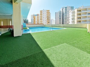 A rooftop pool with artificial grass, surrounded by high-rise buildings. - Gray Apartment Praia Rocha (Portimão)