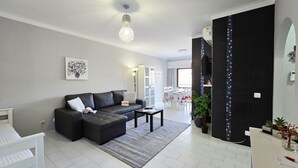 A modern living room with a sectional sofa, a dining area with a table and chairs, and a kitchen area with a counter and cabinets. - Gray Apartment Praia Rocha (Portimão)