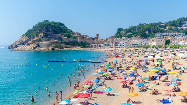 Una spiaggia affollata, con molti ombrelloni e persone che si godono il mare.