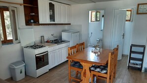 Eine kleine Küche mit weißen Schränken, einem Gasherd und einem Spülbecken. Es gibt einen Holztisch mit Stühlen.