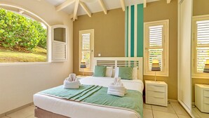 Ein Schlafzimmer mit einem Bett, zwei Nachttischen, einem Fenster mit Rollläden und Blick ins Grüne.