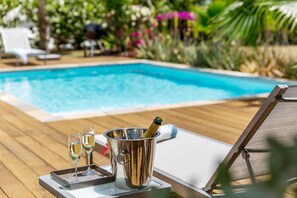 A poolside area with a wooden deck, lounge chairs, and a metal bucket containing a bottle and glasses.
