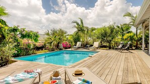 Eine Holzterrasse mit Pool, Liegestühlen und einem Hut auf einem Stuhl.
