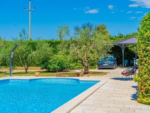 Una piscina con bordo piastrellato, immersa nel verde e con un gazebo.