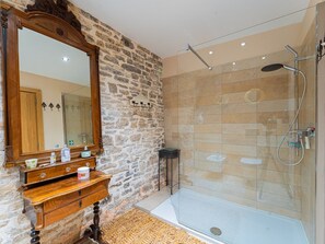 Un bagno con parete in pietra, mobile lavabo in legno, ampio specchio, cabina doccia in vetro e vasca da bagno.