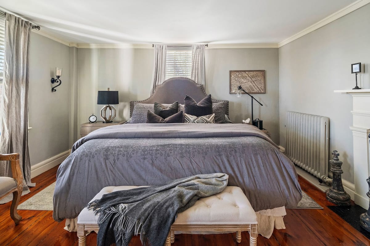 A bedroom with a large bed, a bedside table with a lamp, a radiator, and a picture on the wall.