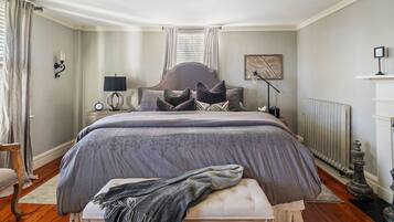 A bedroom with a large bed, a bedside table with a lamp, a radiator, and a picture on the wall.