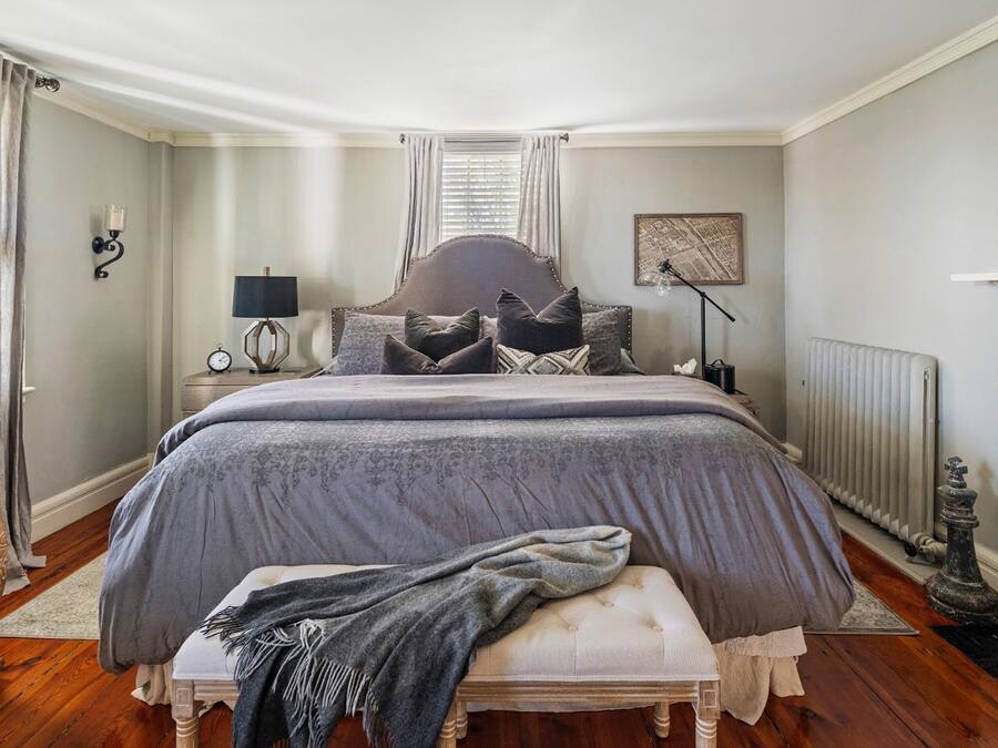 A bedroom with a large bed, a bedside table with a lamp, a radiator, and a picture on the wall.