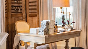 A wooden desk with a lamp, books, decorative items, and a chair in a room with wooden shutters and a window. - The Watson Boutique Bed & Breakfast (Thompson)
