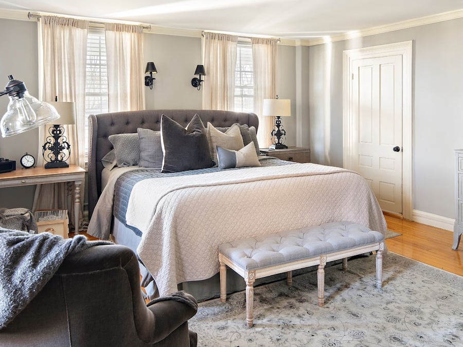 A bedroom with a large bed, bedside lamps, a bench, and a desk with a lamp.