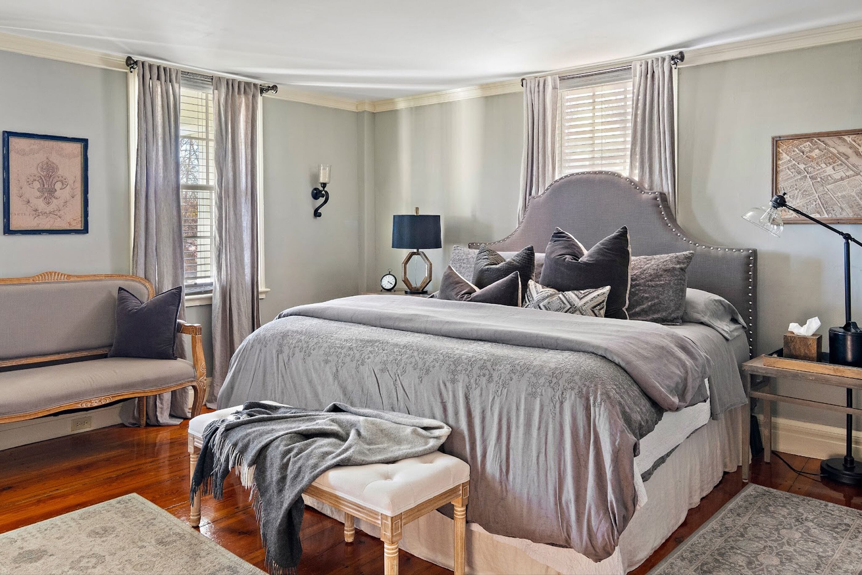A bedroom with a large bed, a bench, a nightstand, a lamp, and a wall clock.