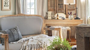 A cozy room with a wooden sofa, a small table with books and a lamp, and a window with curtains. - The Watson Boutique Bed & Breakfast (Thompson)