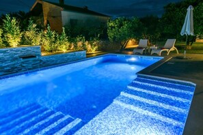 A swimming pool with a tiled edge, surrounded by a stone wall and plants. There are lounge chairs and an umbrella in the background. - Apartment in Okrug Gornji with Seaview, Terrace, Air condition, WIFI (5209-4) (Okrug Gornji)