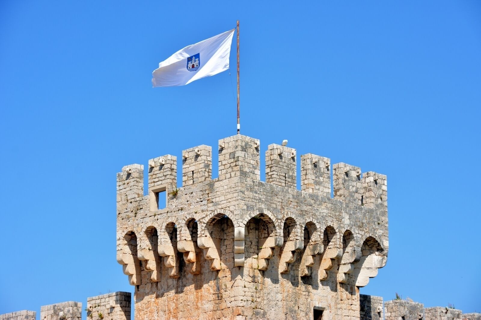 A historic stone castle with a flag on top, featuring multiple arched windows and battlements.