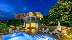 Une maison à deux étages avec une piscine, un espace extérieur aménagé et un mur en pierre.