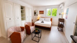 Un dormitorio con cama, dos sillones, una mesita, un espejo y una ventana.