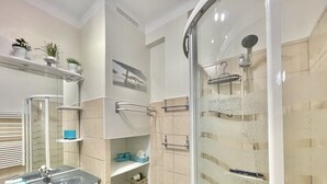 A modern bathroom with a glass shower enclosure, a sink with a marble countertop, and shelves with toiletries. - Magellan (Cannes)