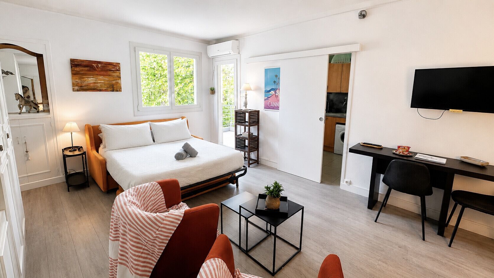 A modern hotel room with a bed, a desk, a chair, a small table, and a TV.
