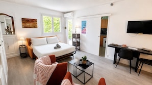 A modern hotel room with a bed, a desk, a chair, a small table, and a TV. - Magellan (Cannes)