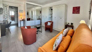 A living room with a sofa, armchair, and ottoman. There is a dining area with a table and chairs. A large mirror reflects the room. - Magellan (Cannes)