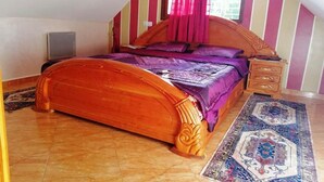 Ein Schlafzimmer mit einem hölzernen Bett, einem Nachttisch, einem Fenster mit Vorhängen und einem gemusterten Teppich.