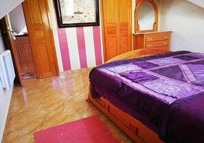A bedroom with a wooden bed, a red rug, a wooden wardrobe, and a map on the wall.