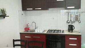 Une cuisine compacte équipée d’une cuisinière à gaz, d’un évier et d’un lave-vaisselle. On y trouve une table à manger avec des chaises, ainsi qu’une petite étagère où sont disposés des objets décoratifs.