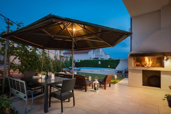 An outdoor patio with a table and chairs, a covered area, and a fireplace.