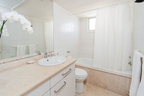 A bathroom with a sink, mirror, toilet, and bathtub.