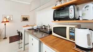Een kleine keuken met een magnetron, broodrooster, waterkoker en een klein fornuis.