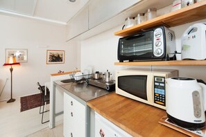 A compact kitchenette with a microwave, toaster, kettle, and a small stove.