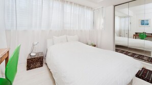 Een slaapkamer met een groot bed, een nachtkastje met een lamp, een groene stoel en een spiegel.