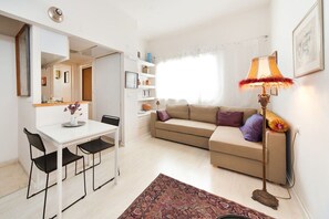 A modern living room with a sofa, a dining table with chairs, a lamp, and a patterned rug.