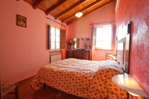A bedroom with a wooden ceiling, a bed with floral bedding, a dresser with a mirror, and a window with curtains. - La Sella - Holiday Home in Tuscany with private pool (Pescaglia)