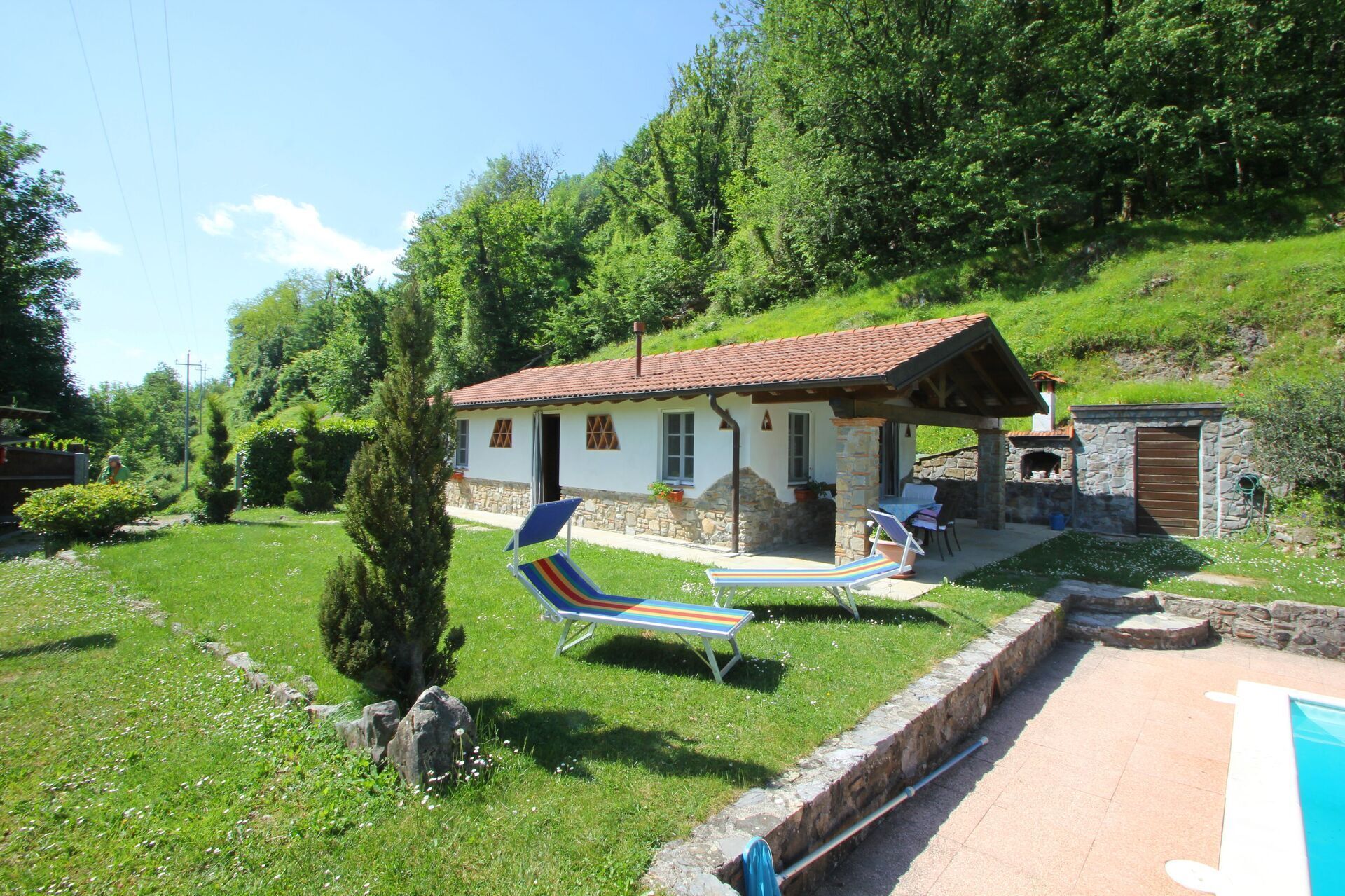 A rustic house with a stone chimney, a stone oven, and a pool area.