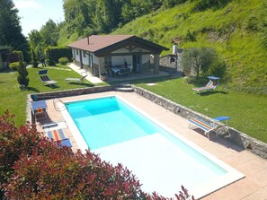 A swimming pool with lounge chairs, a stone house, and a grassy hillside. - La Sella - Holiday Home in Tuscany with private pool (Pescaglia)
