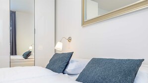A hotel room with a bed, two pillows, a nightstand with a lamp, and a mirror on the wall.