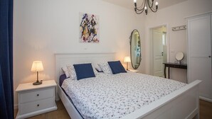 Quarto com cama, mesas de cabeceira, candelabro, espelho e porta.