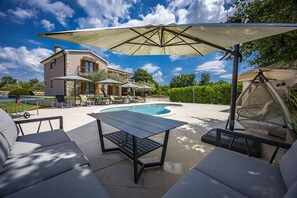 A poolside area with outdoor furniture, a pool, and a house in the background.