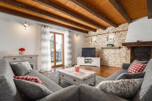 Una sala de estar con pared de piedra, vigas de madera, chimenea y televisor.