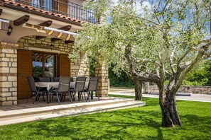 Un edificio de piedra con un patio, mobiliario exterior y un árbol.